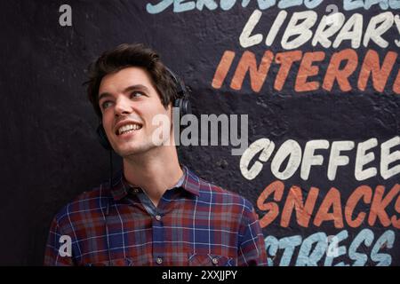 Kopfhörer, Mann und Musik an der Wand zum Entspannen, Podcast oder Radio in der Bibliothek. Audio, Sound und Person in der Stadt für Hip-Streaming Stockfoto