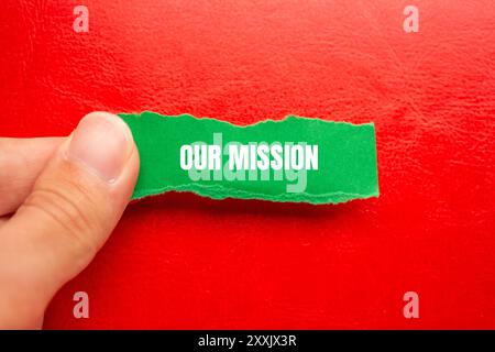 Unsere Botschaft auf gerissenem, gerissenem grünem Papier mit rotem Hintergrund. Konzeptionelles unser Missionssymbol. Kopierbereich. Stockfoto