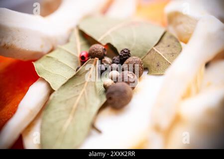 Farbenfrohe Auswahl an Lorbeerblättern, gemischten Pfefferkörnern und frischen Gemüsescheiben, die kreativ angeordnet sind und eine lebendige Palette zum Kochen von Enthusi bieten Stockfoto