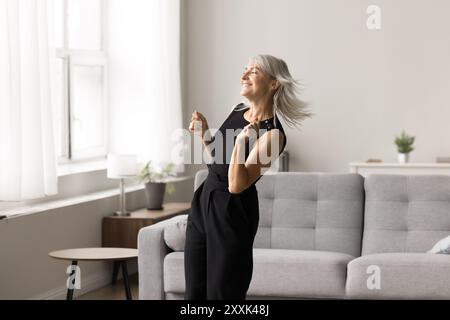 Sorglose reife Frau tanzt, genießen Sie das Wochenende im modischen Wohnzimmer Stockfoto