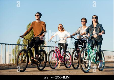 Freunde auf Fahrrädern. Vier junge Leute, die mit dem Fahrrad fahren und lächeln Stockfoto