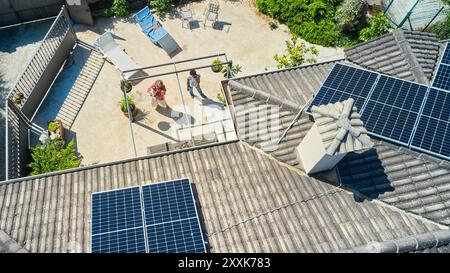Ein Blick aus der Vogelperspektive zeigt zwei Frauen, die in einem Hinterhof stehen und die auf dem Dach installierten Solarpaneele bewundern. In der Szene werden die umweltfreundlichen und n hervorgehoben Stockfoto