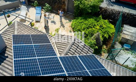 Ein Blick aus der Luft zeigt zwei Frauen in einem sonnigen Hinterhof, eine ist im Garten, während die andere plaudert. Das Dach ist mit Solarpaneelen ausgestattet, Highlight Stockfoto