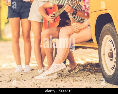 Glückliche Zeit mit Freunden. Nahaufnahme einer Gruppe junger Leute, die Zeit zusammen in der Nähe ihres Kleinwagens verbringen, während ein Mann Gitarre spielt Stockfoto