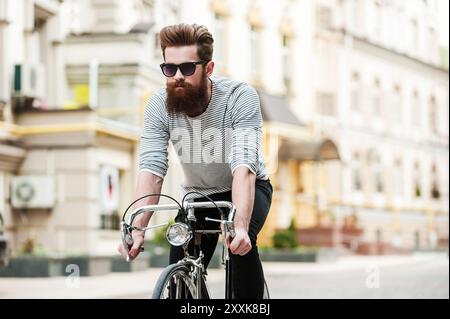 Genießen Sie seine Fahrt. Selbstbewusster junger bärtiger Mann, der sich auf seinem Fahrrad auf der Straße freut Stockfoto