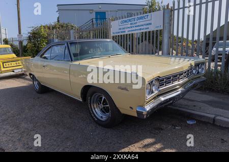 Rayleigh, Großbritannien. August 2024. Ein gut erhaltener gelber Plymouth Road Runner, der in der Nähe einer Fertigbetonfabrik in Großbritannien parkte. Die Gegenüberstellung des Oldtimer-amerikanischen Muscle Car mit der Gebrauchsgegenstände in der industriellen Umgebung unterstreicht Kontraste in Design, Ära und Zweck. Amerikanisches Auto und Truck treffen sich in der Farm Fresh Garage. Bei der Veranstaltung können die Besitzer ihre Fahrzeuge mitbringen, damit die Besucher einen Blick aus der Nähe werfen können. Penelope Barritt/Alamy Live News Stockfoto
