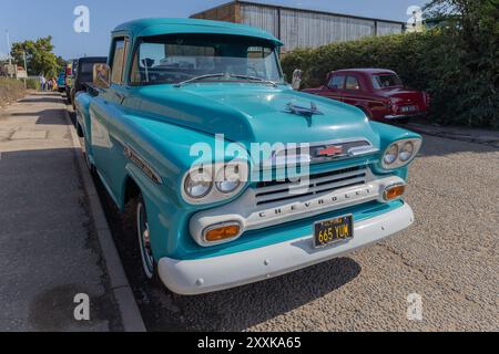 Rayleigh, Großbritannien. August 2024. Ein klassischer, türkisfarbener Chevrolet Apache Pickup-Truck mit Doppelscheinwerfer, verchromtem Kühlergrill und weißem Stoßfänger, der auf einer britischen Straße geparkt ist. Ein roter Oldtimer und Grün im Hintergrund erinnern an den Charme des Autos aus der Mitte des 20. Jahrhunderts. Amerikanisches Auto und Truck treffen sich in der Farm Fresh Garage. Bei der Veranstaltung können die Besitzer ihre Fahrzeuge mitbringen, damit die Besucher einen Blick aus der Nähe werfen können. Penelope Barritt/Alamy Live News Stockfoto
