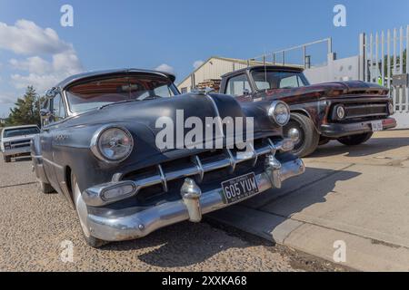 Rayleigh, Großbritannien. August 2024. Ein schwarzer Buick aus den 1950er Jahren und ein rot-schwarzer Pickup aus den 1960er Jahren parkten auf einer Straße in der Nähe eines Lagerhauses und einer Metallzäune. Die nostalgischen Fahrzeuge stehen im Kontrast zum modernen industriellen Umfeld und erinnern an Themen des Kulturerbes und des urbanen Wandels. Amerikanisches Auto und Truck treffen sich in der Farm Fresh Garage. Bei der Veranstaltung können die Besitzer ihre Fahrzeuge mitbringen, damit die Besucher einen Blick aus der Nähe werfen können. Penelope Barritt/Alamy Live News Stockfoto