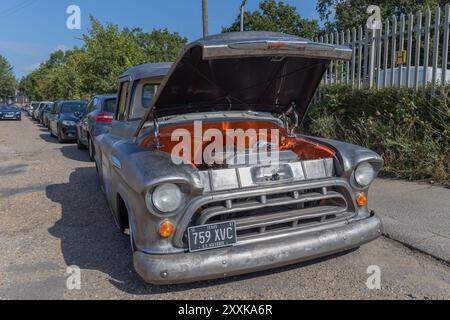 Rayleigh, Großbritannien. August 2024. Ein amerikanischer Pickup-Truck aus der Mitte des 20. Jahrhunderts mit verwittertem Metallic-Äußere steht auf einem Industriegelände mit geöffneter Motorhaube, wodurch der Motor sichtbar wird. Das Fahrzeug steht im Gegensatz zu modernen Fahrzeugen in der Umgebung, was eine Restaurierung oder Wartung andeutet. Amerikanisches Auto und Truck treffen sich in der Farm Fresh Garage. Bei der Veranstaltung können die Besitzer ihre Fahrzeuge mitbringen, damit die Besucher einen Blick aus der Nähe werfen können. Penelope Barritt/Alamy Live News Stockfoto