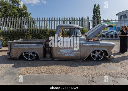 Rayleigh, Großbritannien. August 2024. Ein stark modifizierter Vintage-Pickup-Truck mit abgesenkter Federung, großen Chromrädern und verwittertem Metallic-Finish, parkt in der Nähe eines Metallzaun. Die Motorhaube ist geöffnet, was auf Anzeige oder Wartung hinweist. Das Branding auf der Seite lautet „WAMPLER – Wings of Custom“. Amerikanisches Auto und Truck treffen sich in der Farm Fresh Garage. Bei der Veranstaltung können die Besitzer ihre Fahrzeuge mitbringen, damit die Besucher einen Blick aus der Nähe werfen können. Penelope Barritt/Alamy Live News Stockfoto