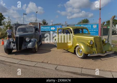 Rayleigh, Großbritannien. August 2024. Zwei restaurierte Oldtimer aus den 1930er Jahren, ein mattes Grau und ein metallisches Gelbgrün. Die Gegenüberstellung von klassischem Automobildesign vor einem modernen industriellen Hintergrund hebt Themen wie Restaurierung, Nostalgie und britische Motorsport-Tradition hervor. Amerikanisches Auto und Truck treffen sich in der Farm Fresh Garage. Bei der Veranstaltung können die Besitzer ihre Fahrzeuge mitbringen, damit die Besucher einen Blick aus der Nähe werfen können. Penelope Barritt/Alamy Live News Stockfoto