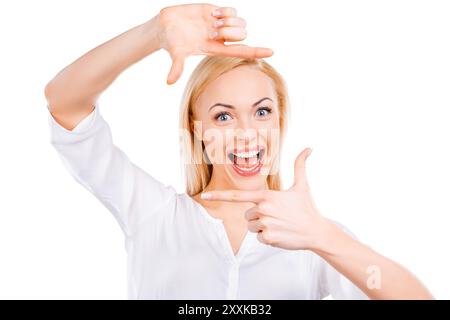 Porträt des Glücks. Glückliche junge Frau mit blondem Haar, die auf Kamera und Fingerrahmen blickt, während sie vor weißem Hintergrund steht Stockfoto