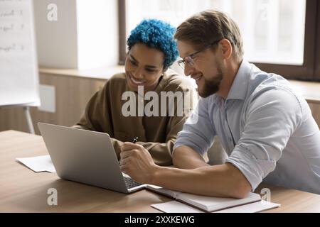 Zwei Kollegen, die am Schreibtisch sitzen und an einem Projekt mithilfe eines Laptops arbeiten Stockfoto