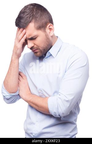 Erschöpft. Seitenansicht eines jungen Mannes im Hemd, der seinen Kopf berührt und die Augen geschlossen hält, während er vor weißem Hintergrund steht Stockfoto