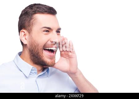 Gute Neuigkeiten! Fröhlicher junger Mann in formaler Kleidung, der die Hand nahe dem Mund hält und vor weißem Hintergrund schreien kann Stockfoto