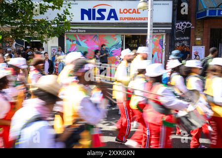 NUR Carnival-Besucher vor einem Kunstwerk des lokalen Straßenkünstlers CEE im Nisa-Shop in Ladbroke Grove, London. Bilddatum: Sonntag, 25. August 2024. Hennessy hat sich mit einer Reihe unabhängiger Eckläden entlang der Paraderoute zusammengetan, um den Notting Hill Carnival und die Markteinführung der limitierten Flasche zu feiern. Das Foto sollte lauten: Matt Crossick/PA Media Assignments Stockfoto