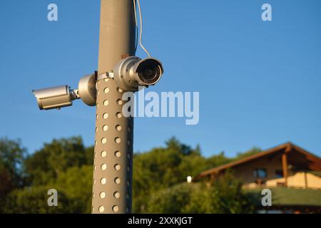 Zwei Überwachungskameras auf einem Stab mit einem Haus im Hintergrund unter einem klaren blauen Himmel. Sicherheitsüberwachungskonzept für den Außenbereich. Stockfoto