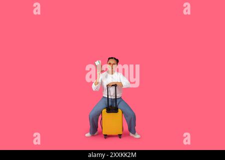 Frau mit gelbem Koffer und Fahrkarte auf rosa Hintergrund Stockfoto
