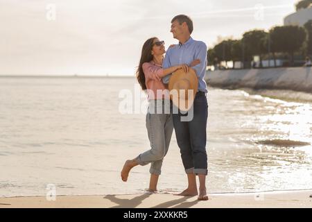 Ein Paar genießt einen romantischen Strandspaziergang bei Sonnenuntergang in warmer Küstenlage Stockfoto
