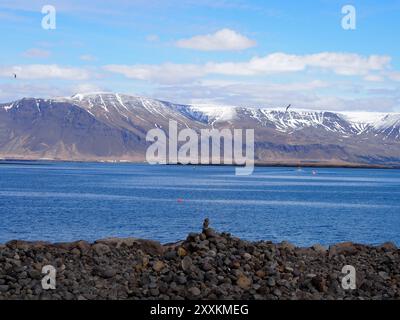 Küstenlandschaft mit einer felsigen Küste, die zu einem ruhigen, weitläufigen Ozean führt, mit schneebedeckten Bergen, die eine atemberaubende Kulisse unter einer ruhigen Kulisse schaffen Stockfoto