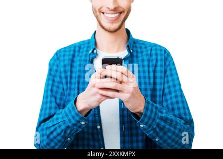 Die richtigen Wörter auswählen. Nahaufnahme eines jungen Mannes im Hemd, der Handy hält und lächelt, während er vor weißem Hintergrund steht Stockfoto