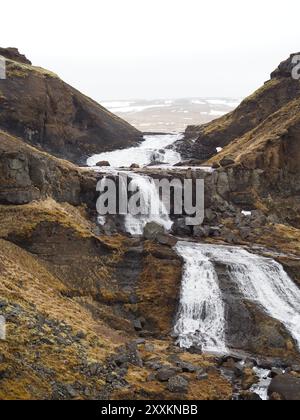 Ein Berghang mit kleinen Wasserfällen und einem Bach, der über dunkle Felsen fließt und die kraftvolle Bewegung des Wassers durch ein raues und natürliches lan erfasst Stockfoto