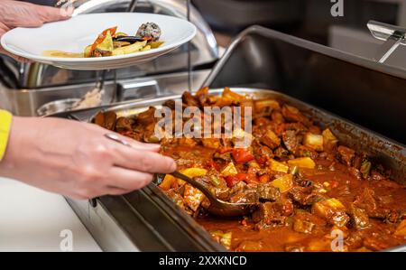 Die Frau legt Essen auf den Teller am Buffet. All-inclusive-System. Stockfoto