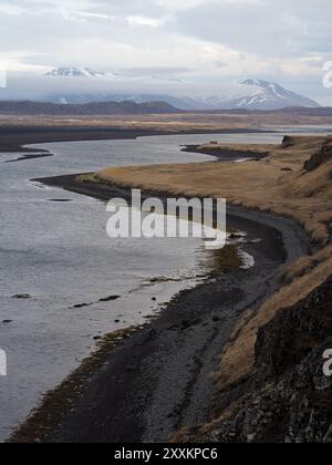 Ein sich windender Fluss fließt durch eine karge Landschaft mit weit entfernten, schneebedeckten Bergen und fängt eine ruhige und abgelegene Naturszene mit rauer Schönheit ein Stockfoto