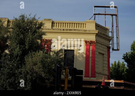 Der Rahmen eines aufwendigen, alten beleuchteten Schildes über der Vorderseite eines viktorianischen Gebäudes, das von Straßenbäumen in Perth, Western Australia, eingerahmt wird Stockfoto