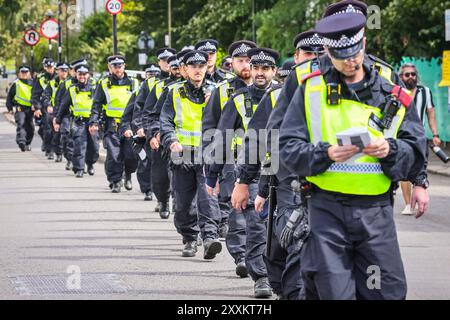 London, Großbritannien. August 2024. Polizisten bilden eine Linie auf dem Weg zu ihrer Position. Der Karnevalssonntag in Notting Hill beginnt mit der traditionellen Polizeieinheit, die eine Linie bildet, um zu ihren Positionen zu gehen. Kinderkarneval und eine familienorientierte Karnevalsparade. Am ersten von zwei Tagen des Karnevalsfestes in Notting Hill feiern die Nachtschwärmer dieses Wochenende an der Karnevalsroute an Soundsystemen, Ständen und Veranstaltungsorten. Quelle: Imageplotter/Alamy Live News Stockfoto