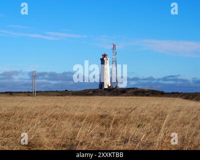 Ein Leuchtturm und ein Kommunikationsturm stehen zusammen in einem weiten, trockenen Feld unter einem klaren blauen Himmel, die Isolation und Führung in einem natura darstellen Stockfoto