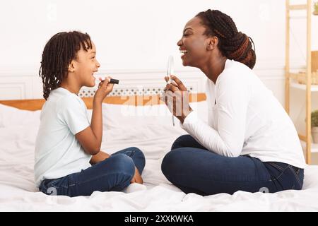 Kleines afro-Mädchen, das mit ihrer Mutter im Schlafzimmer Make-up macht Stockfoto