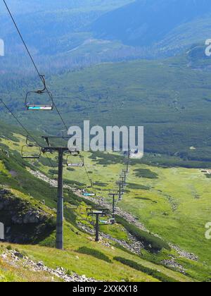 Ein malerischer Sessellift, der sich über ein riesiges, grünes Tal mit weit entfernten Bergen im Hintergrund erstreckt und einen wunderschönen und ruhigen Blick auf die natürliche Landschaft bietet Stockfoto