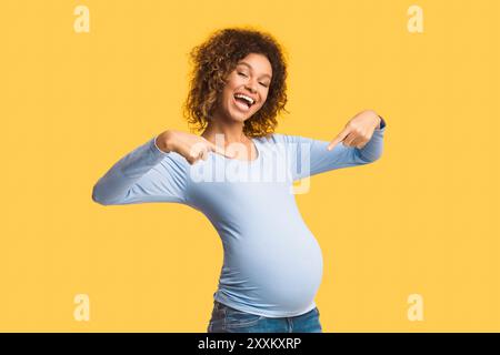 Emotional schwangere Frau lächelt und zeigt mit den Fingern auf den Bauch Stockfoto