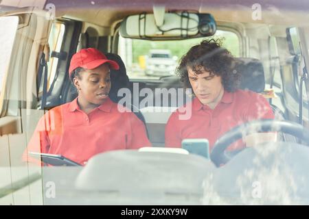 Menschen in roten Uniformen arbeiten im Lieferfahrzeug zusammen, besprechen Lieferpläne und prüfen Dokumente vor dem Fahrzeugsitz Stockfoto