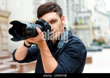 Bereit für die Aufnahme. Selbstbewusster junger Mann, der etwas fotografiert, während er draußen steht Stockfoto