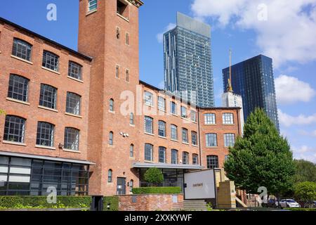 Manchester, Greater Manchester, Großbritannien. 24. August 2024: Renoviertes Industriehaus mit modernen Hochhäusern im Hintergrund an einem sonnigen Tag. Stockfoto