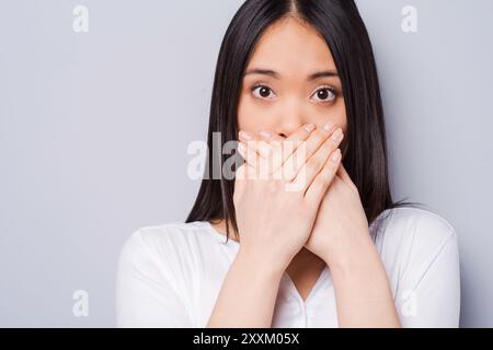 Oops! Überrascht junge asiatische Frau, Mund, Hände und starrte auf Kamera, während gegen grauen Hintergrund stehend Stockfoto