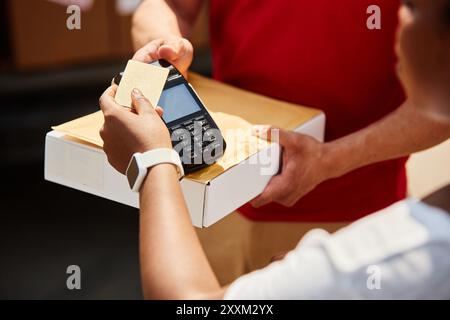 Nahaufnahme der Hände einer Person, die Kreditkartenzahlungen mit Kartenleser mit Box auf der Theke durchführt, weiße Smartwatch am Handgelenk trägt, die eine moderne Einzelhandelsbörse veranschaulicht Stockfoto