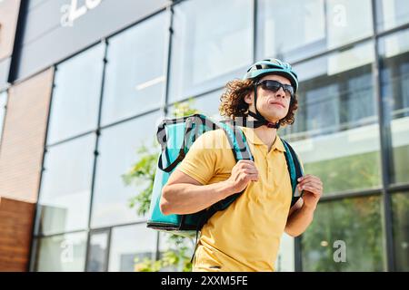 Kurier fährt Fahrrad auf der modernen Stadtstraße mit grünem Rucksack und Helm und Sonnenbrille bei hellem Sonnenlicht Stockfoto