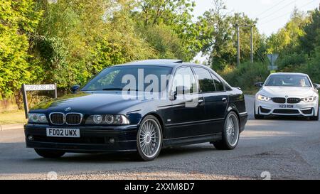 Whittlebury, Northants., Großbritannien - 25. August 2024: Zwei BMW-Autos fahren auf einer britischen Landstraße. Ein 2002er BMW Alpina in Schwarz und ein 2016er BMW M4 in weiß Stockfoto