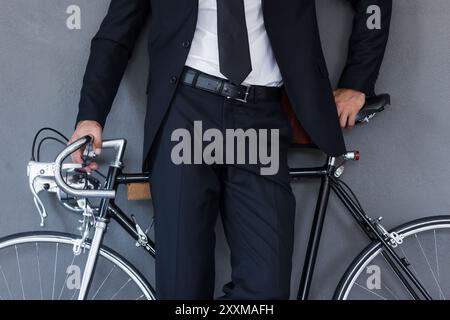 Geschäftsmann mit Fahrrad. Nahaufnahme eines Geschäftsmannes, der sich an das Fahrrad lehnt, während er vor grauem Hintergrund steht Stockfoto