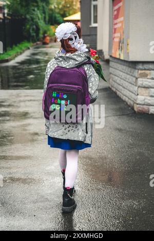 Ein Schulmädchen geht am 1. September mit Blumen und einem Rucksack mit der Aufschrift Hello School zur Schule Stockfoto