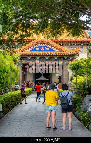 Die Menschen laufen auf einem Pfad durch einen Garten, der sich einem der farbenfrohen Tempel im Kek Lok Si Temple Complex in Penang, Malaysia, nähert Stockfoto