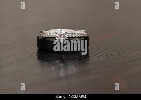 Braut und Bräutigam Eheringe gestapelt. Schwarzer Bräutigam-Ring und Bräute Weißgold mit Diamanten auf reflektierendem Holztisch. Stockfoto