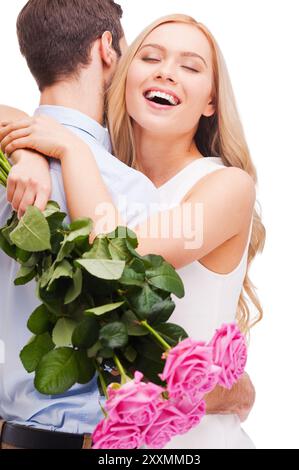 Ich liebe dich so sehr! Wunderschönes junges, liebevolles Paar, das sich umarmt, während die Frau einen Strauß rosa Rosen hält und lächelt und beide isoliert auf weißem Ba stehen Stockfoto