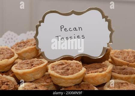 Schönes weißes Schild mit goldenem Rand, auf dem "Pecan Tassies" auf einem Stapel köstlicher Desserts steht Stockfoto