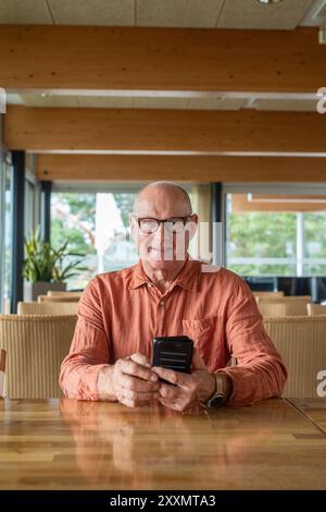 Senior Finn Mann, der während des Herbstkonzepts das Mobiltelefon im Restaurant benutzt Stockfoto