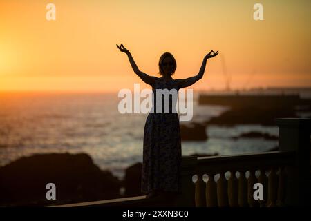 Die Silhouette einer Frau steht an einer Meerespromenade in der Dämmerung. Stockfoto