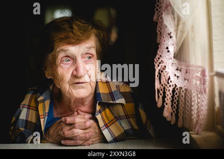 Ein berührendes Porträt einer älteren Frau, die an einem Tisch sitzt. Stockfoto
